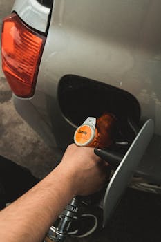 Close-up of a hand refilling a car at a gas station during daylight.